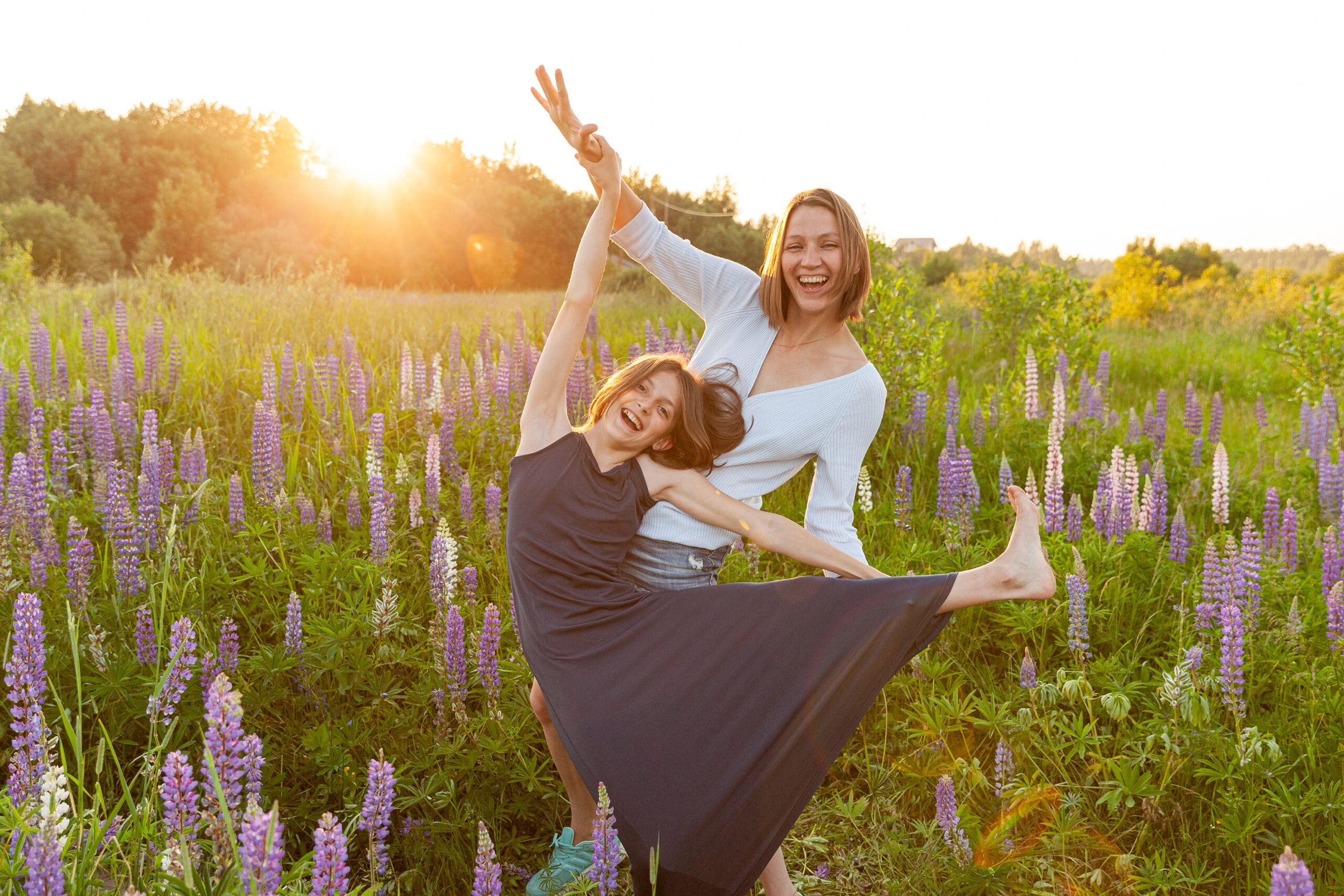 Young mother embracing her child outdoor. Woman and teenage girl on summer field with blooming wild flowers green background. Happy family mom and daughter playing on meadow.